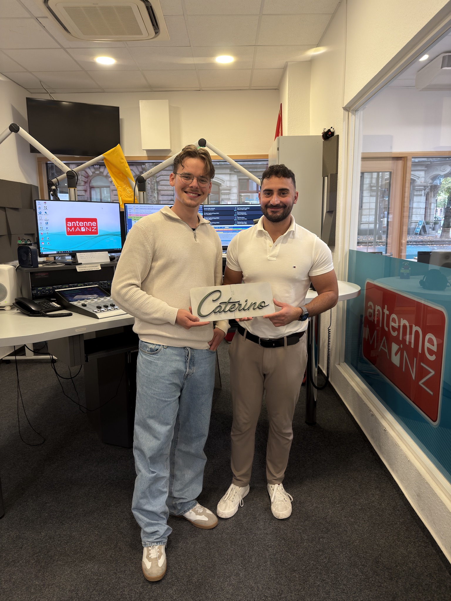 Zwei Personen im Studio von Antenne Mainz mit einem Caterino-Schild